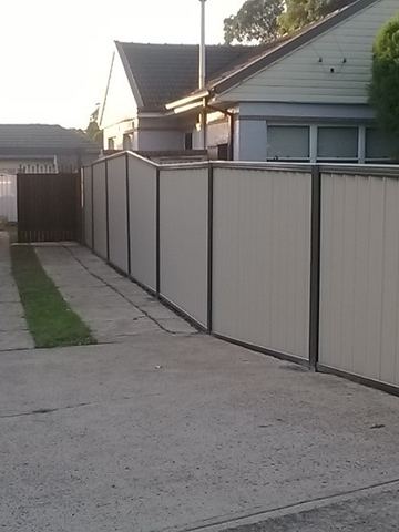 Long cream Colorbond privacy fence running along a driveway to a brick house