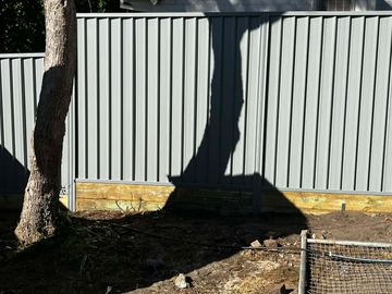 The scene shows a mid grey corrugated steel fence where sleepers form the base.