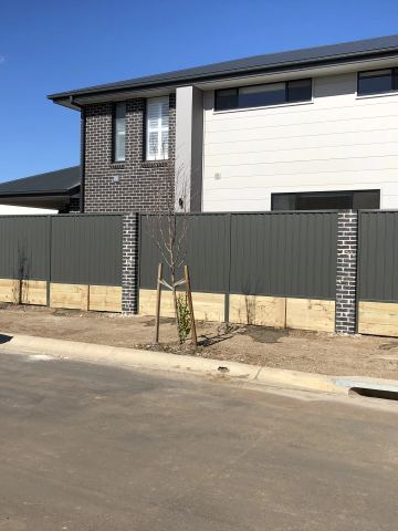 The scene shows a mid grey corrugated steel fence where sleepers form the base.