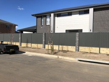 The scene shows a mid grey corrugated steel fence where sleepers form the base.