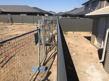 Charcoal Colorbond privacy fence along a dirt yard beside a temporary mesh fence