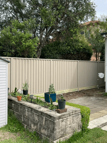 Cream Colorbond privacy fence beside a garden shed and a raised garden bed