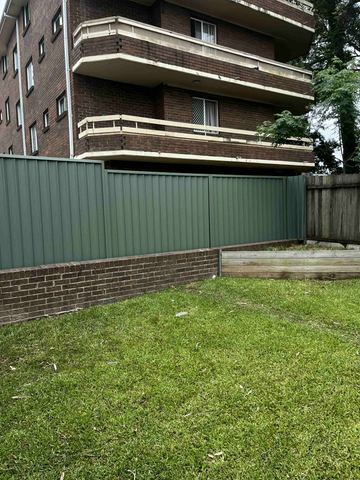 Green Colorbond privacy fence standing on a brick and timber plinth across a lawn