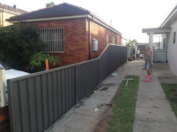 Dark grey Colorbond privacy fence running along a driveway beside a brick house