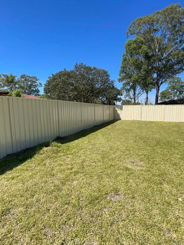 Long cream Colorbond privacy fence stretching across an open lawn