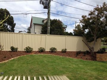 Cream Colorbond privacy fence following a curved mulched garden bed