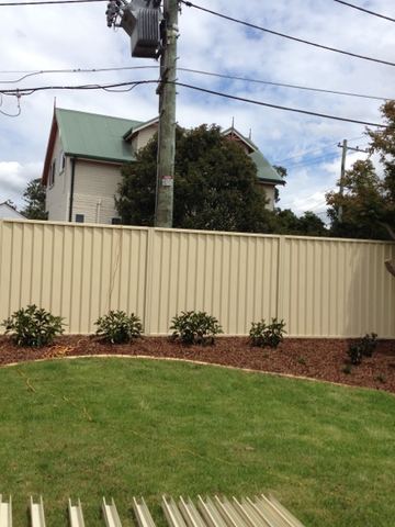 Cream Colorbond privacy fence following a curved mulched garden bed