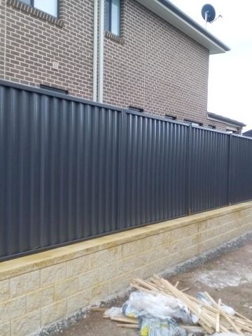 The scene shows a mid grey corrugated steel fence where sleepers form the base.