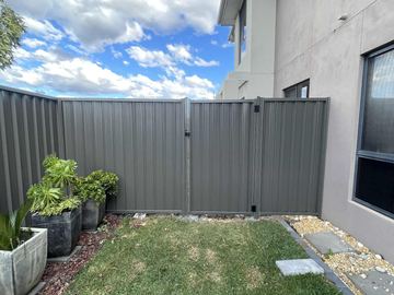 Grey Colorbond privacy fence returning to a rendered house wall beside potted plants on a small lawn