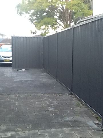 Charcoal Colorbond privacy fence enclosing an empty paved courtyard with a garden hose on the ground
