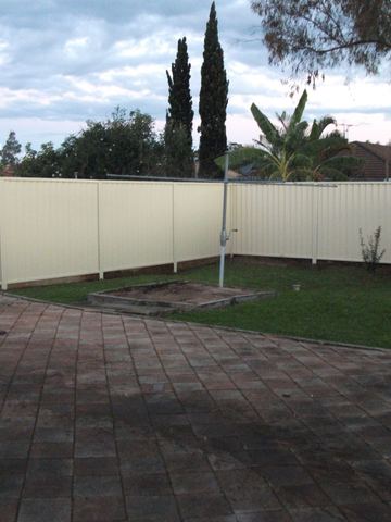 Cream Colorbond privacy fence enclosing a paved backyard