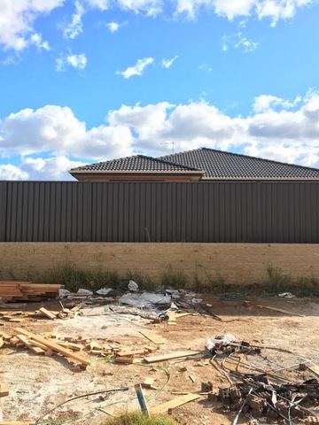 Charcoal Colorbond privacy fence across a dirt yard with timber offcuts on the ground