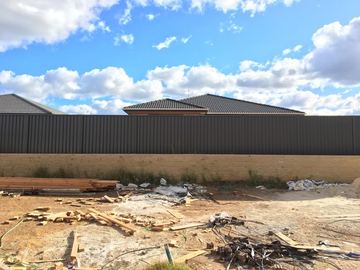 Charcoal Colorbond privacy fence across a dirt yard with timber offcuts on the ground