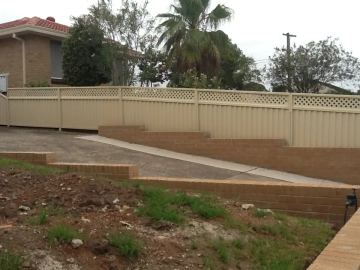 Stepped cream panels topped with diamond lattice follow a sloped garden above tiered brick retaining and a concrete path.