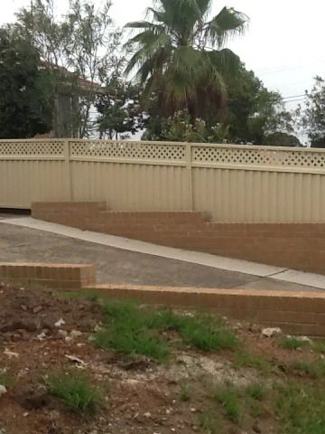 Stepped cream panels topped with diamond lattice follow a sloped garden above tiered brick retaining and a concrete path.