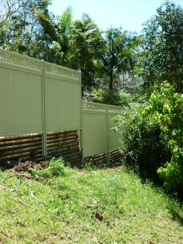 The scene shows a green corrugated steel fence where garden beds sit at the base.