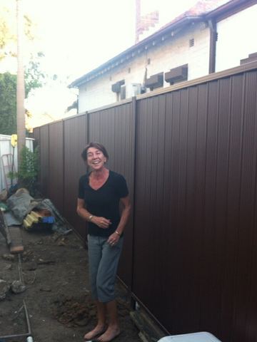 Bronze Colorbond privacy fence in a side yard with a person standing beside it