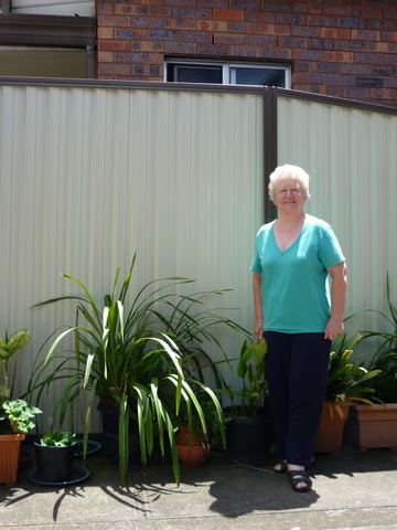 Cream Colorbond privacy fence beside potted garden plants with a person standing in front