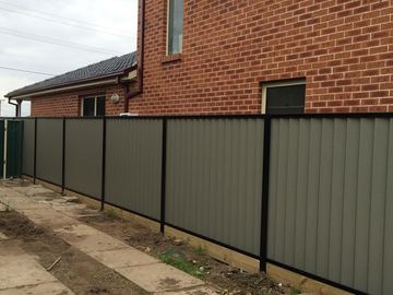 Grey Colorbond privacy fence with black posts beside a brick house