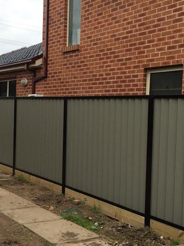 Grey Colorbond privacy fence with black posts beside a brick house