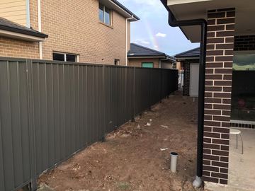 Long charcoal Colorbond privacy fence along the side of a new brick house