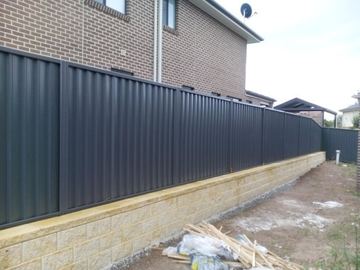 Charcoal Colorbond privacy fence sitting on a pale stone retaining wall