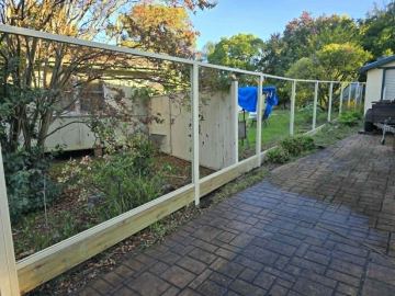 Open cream post-and-rail frames without infill curve along a brick patio and sleeper plinth in a leafy backyard.