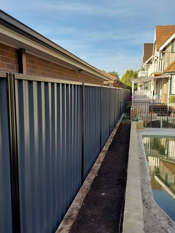 Dark Colorbond privacy fence running along a narrow planted garden bed beside a house