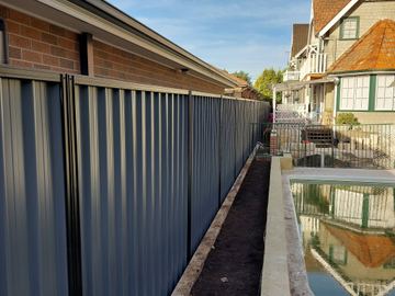 Dark Colorbond privacy fence running along a narrow planted garden bed beside a house