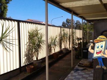 Cream Colorbond privacy fence under a covered patio with potted plants along the line