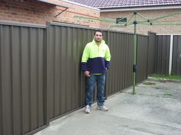 Mid grey Colorbond privacy fence beside a rotary clothesline with an installer standing in front