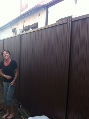 Close view of a bronze Colorbond privacy fence with a person standing beside the sheets