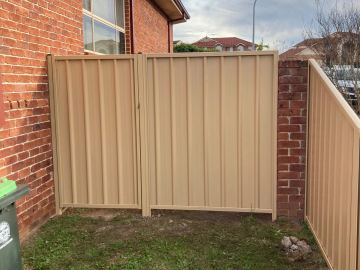 Installed Colorbond sheets sitting on a timber sleeper wall with a matching gate opening.
