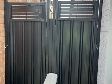 Charcoal panels with slat toppers fill a tight passage between red and white brick walls above pebbles and pavers.