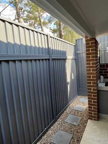 Mid grey Colorbond privacy fence returning to a brick house wall