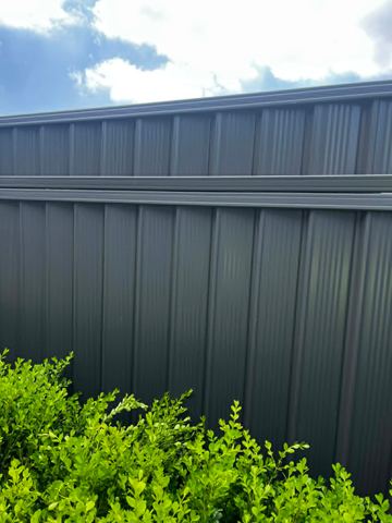 Charcoal panels divided by a mid-rail rise behind a trimmed box hedge under a bright overcast sky.
