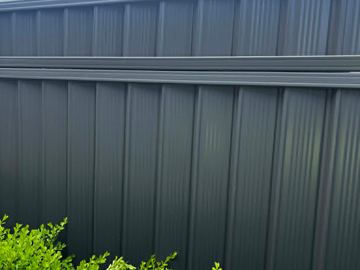 Charcoal panels divided by a mid-rail rise behind a trimmed box hedge under a bright overcast sky.