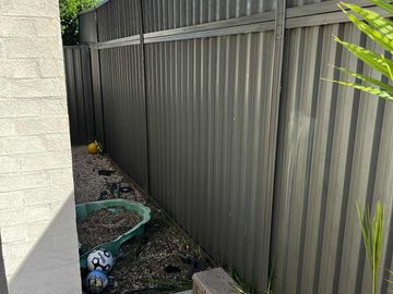 Charcoal panels with a shorter top section line a side yard of pavers, toys and a turtle sandbox beside white brick.