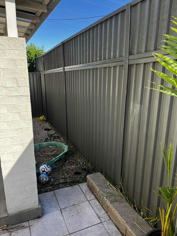 Charcoal panels with a shorter top section line a side yard of pavers, toys and a turtle sandbox beside white brick.