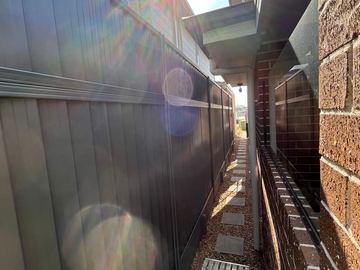 Dark Colorbond privacy fence filling a narrow side passage against a brick house wall