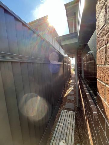 Dark Colorbond privacy fence filling a narrow side passage against a brick house wall