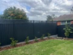 Charcoal lattice-topped panels on concrete sleepers border mulch and small shrubs along a green lawn by brick.