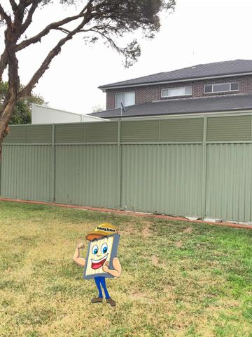 Sage panels with slat tops and brick edging stand before a two-storey brick house and paperbark tree.