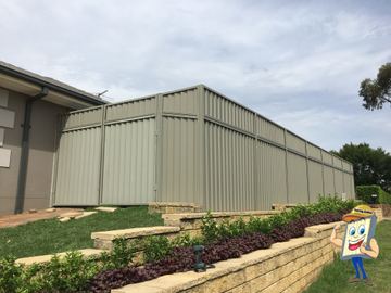 Willow-green panels with a double gate stand above tiered sandstone garden beds with low plantings.
