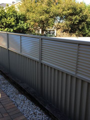 White Colorbond fence with a slat topper running along a street boundary