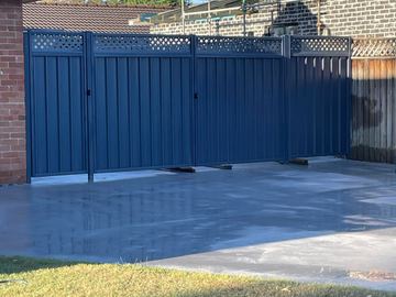 Charcoal panels with diamond lattice and a wide double gate open over fresh concrete near scaffolding.