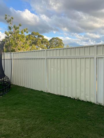 Cream panels with a narrow top band line a lawn with a trampoline edge and cloudy sky above trees.