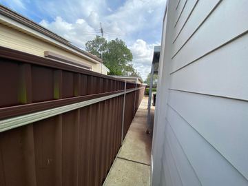 Brown Colorbond privacy fence running beside a white weatherboard house