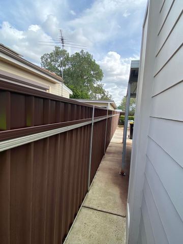 Brown Colorbond privacy fence running beside a white weatherboard house
