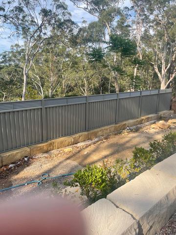 Mid grey Colorbond privacy fence on a sandstone plinth along a bushland boundary